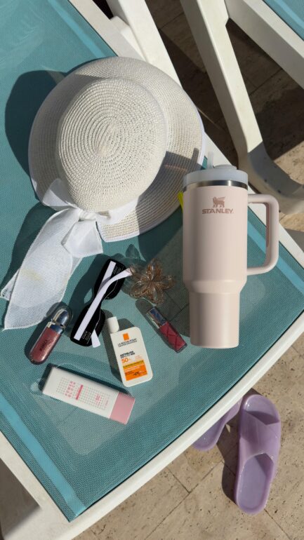 Flat lay of summer accessories on a sunbed, featuring a hat, sunscreen, and stylish bottle.